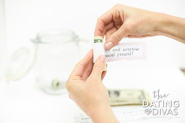 2 hands wrapping paper around dollar bill for date night jar