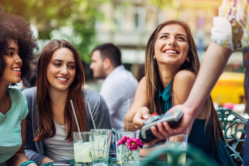 Group of young women paying with credit card in bistro