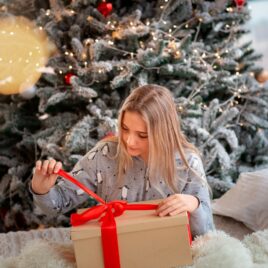 Teenage girl opening gift in front of tree | The Dating Divas