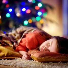 Child sleeping next to lit-up Christmas tree | The Dating Divas