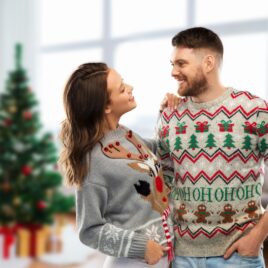 Couple wearing ugly Christmas sweaters in front of decorated tree | The Dating Divas