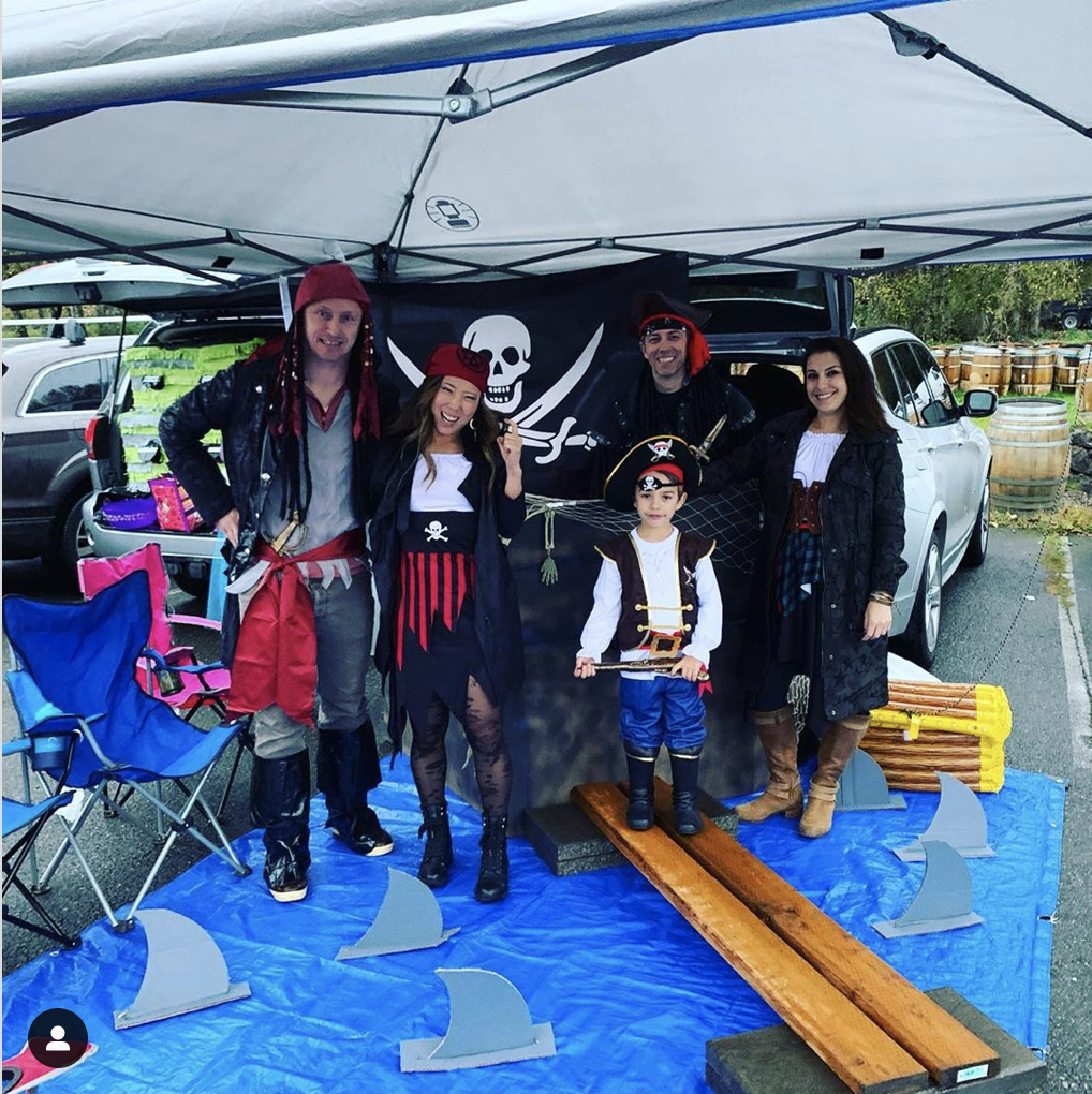 A trunk decorated a pirate ship with a blue tarp laid out in front to create a sea scene (including with sharks!) - a fun trunk or treat decorating idea | The Dating Divas