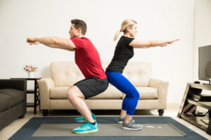 A man and woman doing squats back-to-back at home | The Dating Divas