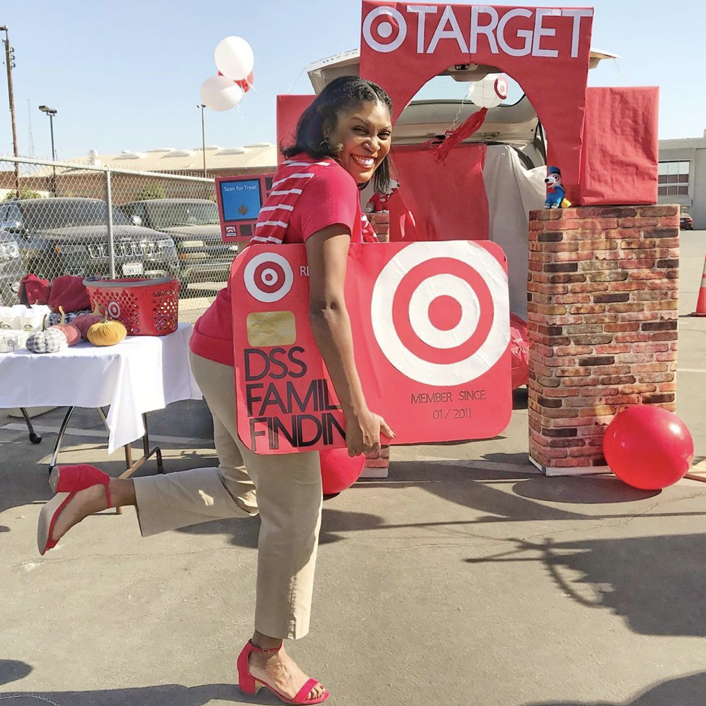 A car trunk decorated as a Target store. A person is dressed as a Target employee carrying an oversized Target Red Card. A fun idea for Trunk or Treat | The Dating Divas