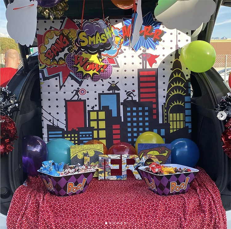 A trunk decorated with a classic building scene from a superhero comic book. There are blue, red and yellow windows and signs. This is such a fun trunk or treat idea for Halloween. | The Dating Divas