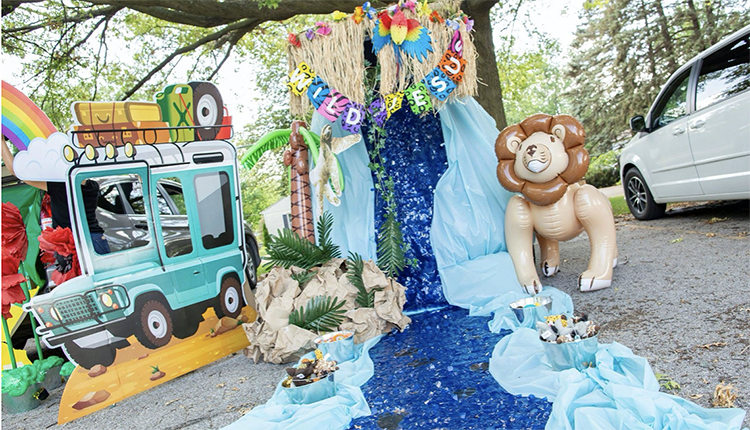 A trunk decorated with a safari jeep cutout and a large waterfall and river made from fabric. An inflatable palm tree and lion add to creating a safari and jungle feel. This is a fun trunk or treat idea for church. | The Dating Divas