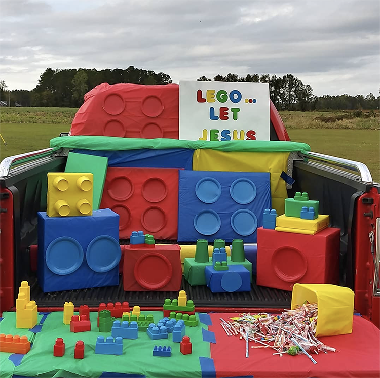 A trunk decorated with legos. The boxes are wrapped in colorful wrapping paper with matching paper places. A sign reads, "Lego and let Jesus" making this an easy trunk or treat idea for a church trunk or treat event. | The Dating Divas