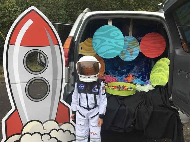 A trunk decorated with planets. The trunk is space with hanging planets and a large rocket ship cut out. A child is dressed as an astronaut to match the car's space trunk or treat theme. | The Dating Divas