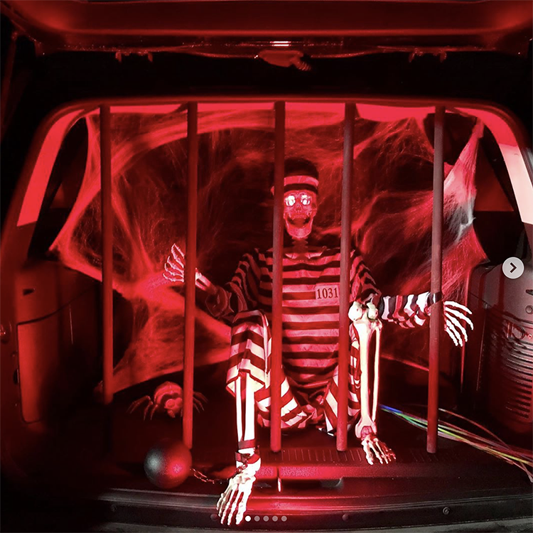 A trunk decorated with red lights lighting a jail cell. Inside the jail is a skeleton. This is a fun idea for a scary trunk or treat theme | The Dating Divas