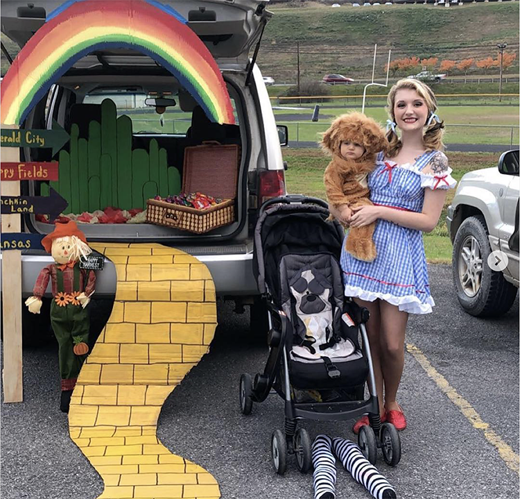 Trunk decorated with a theme for the classic movie The Wizard of Oz. It includes a yellow brick road leading to the car and a large rainbow stretching across the car's trunk. A mother and child are dressed as Dorothy and the Lion - characters from the move. This is a great trunk or treat idea | The Dating Divas