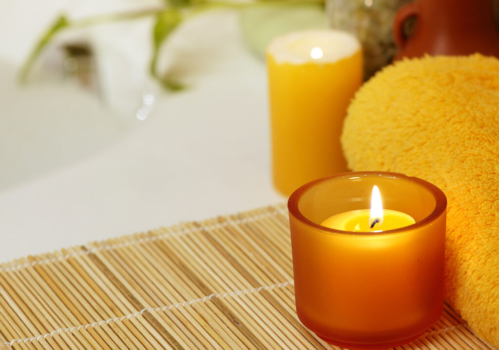 A glowing candle next to a bubble bath showing an example of how to make a DIY spa day at home. | The Dating Divas