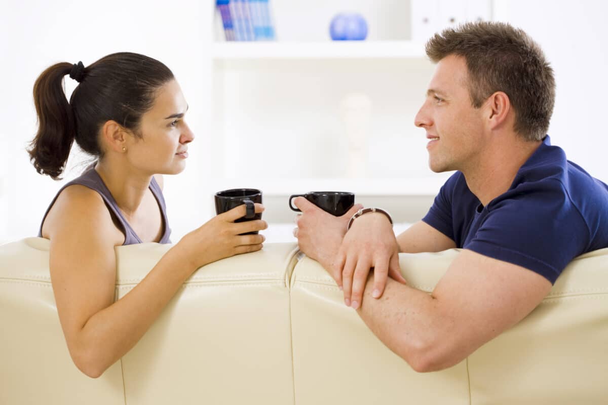 A man and woman communicating together while enjoying coffee at home on the couch | The Dating Divas