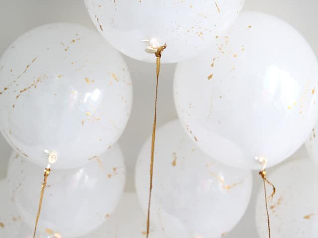 Splatter gold paint onto white balloons for birthday party decorations | The Dating Divas