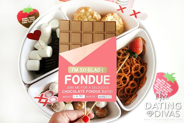Romantic Valentine's Day idea of woman holding "I'm so glad I fondue" sign in front of snack plate | The Dating Divas