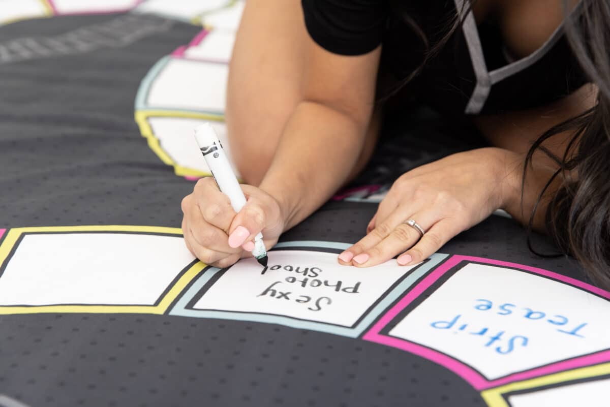 A woman writes a foreplay idea on the Sheets and Ladders bedsheet board game | The Dating Divas