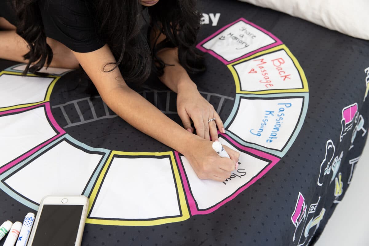 A woman writes foreplay ideas using a washable marker included in the Sheets and Ladders kit | The Dating Divas