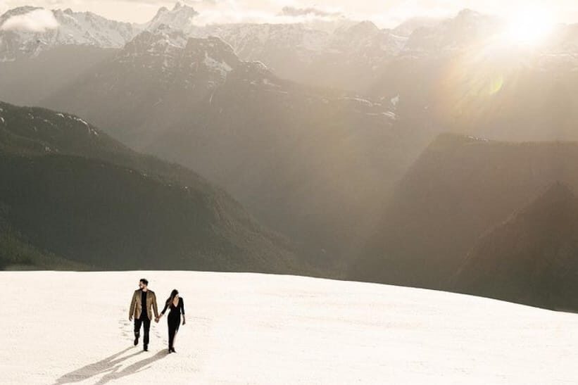 An engaged couple walking on top of a snowy mountaintop during their winter engagement photos | The Dating Divas