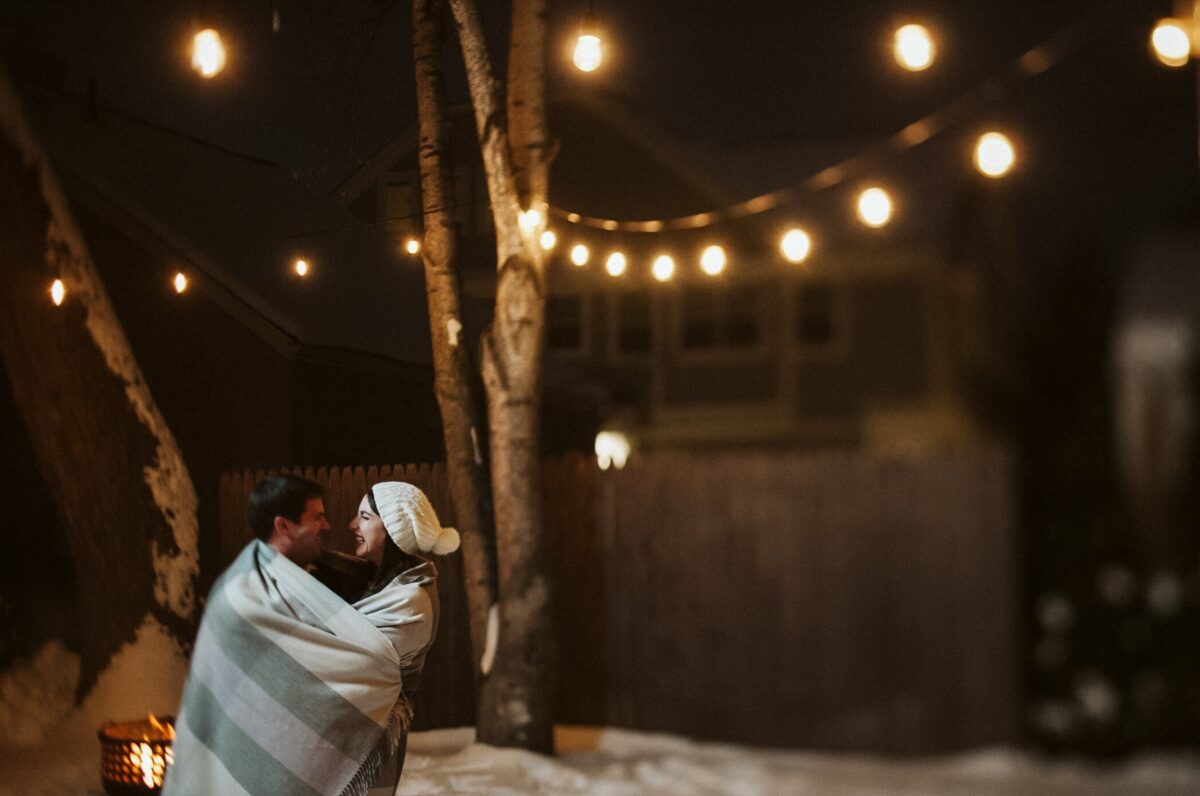 A winter image that shows a man and woman smiling while wrapped in a blanket | The Dating Divas