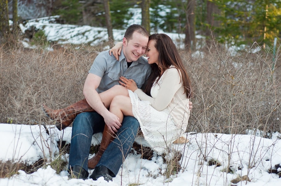 Winter engagement photos featuring a couple sitting in the snow | The Dating Divas