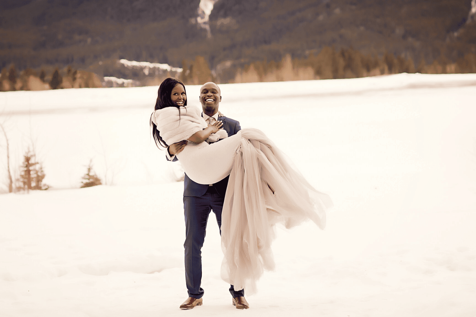 An engaged couple standing in a snowy field during their winter engagement photos | The Dating Divas