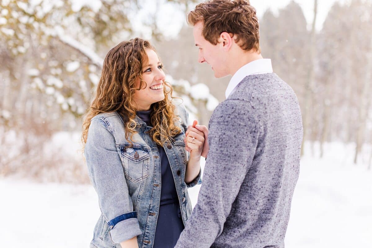 A couple taking winter engagement photos in the snow | The Dating Divas