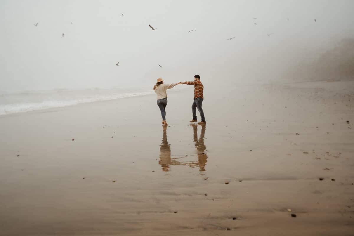 A winter image that shows a couple holding hands and walking on a beach | The Dating Divas