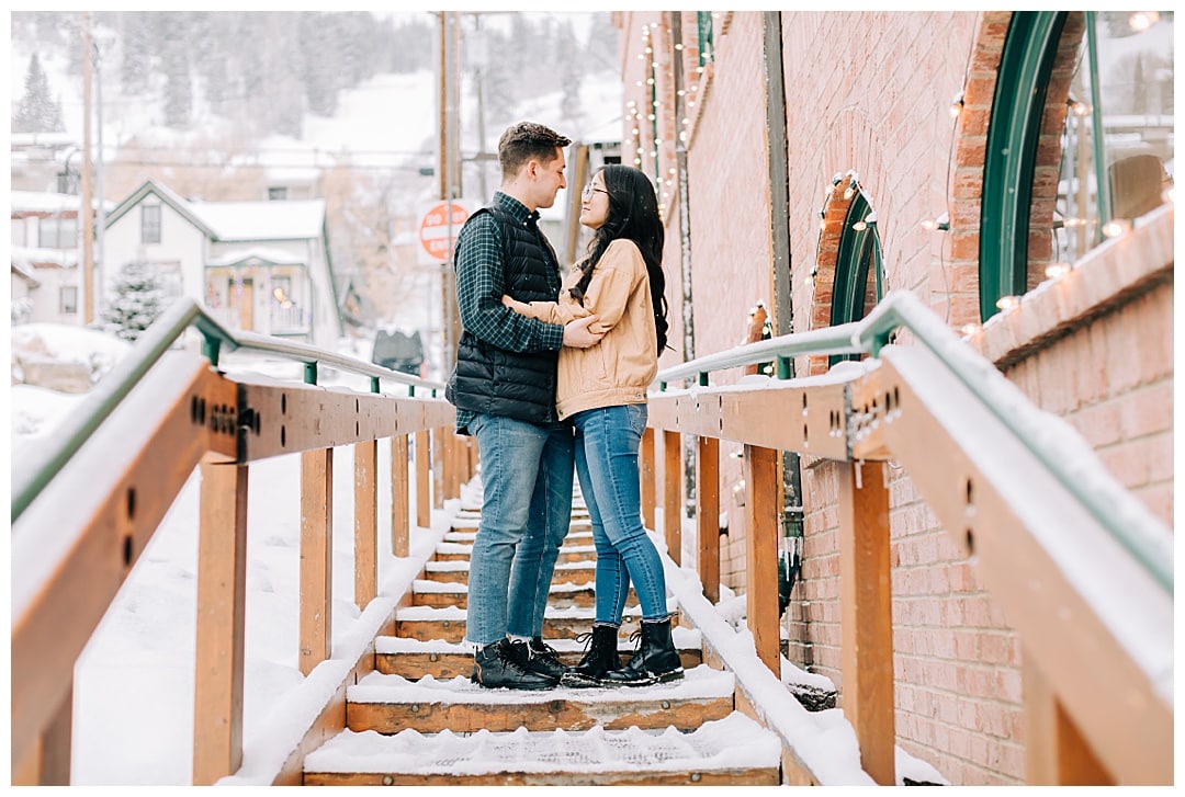 Winter engagement photos where the couple stands on a snowy set of stairs | The Dating Divas