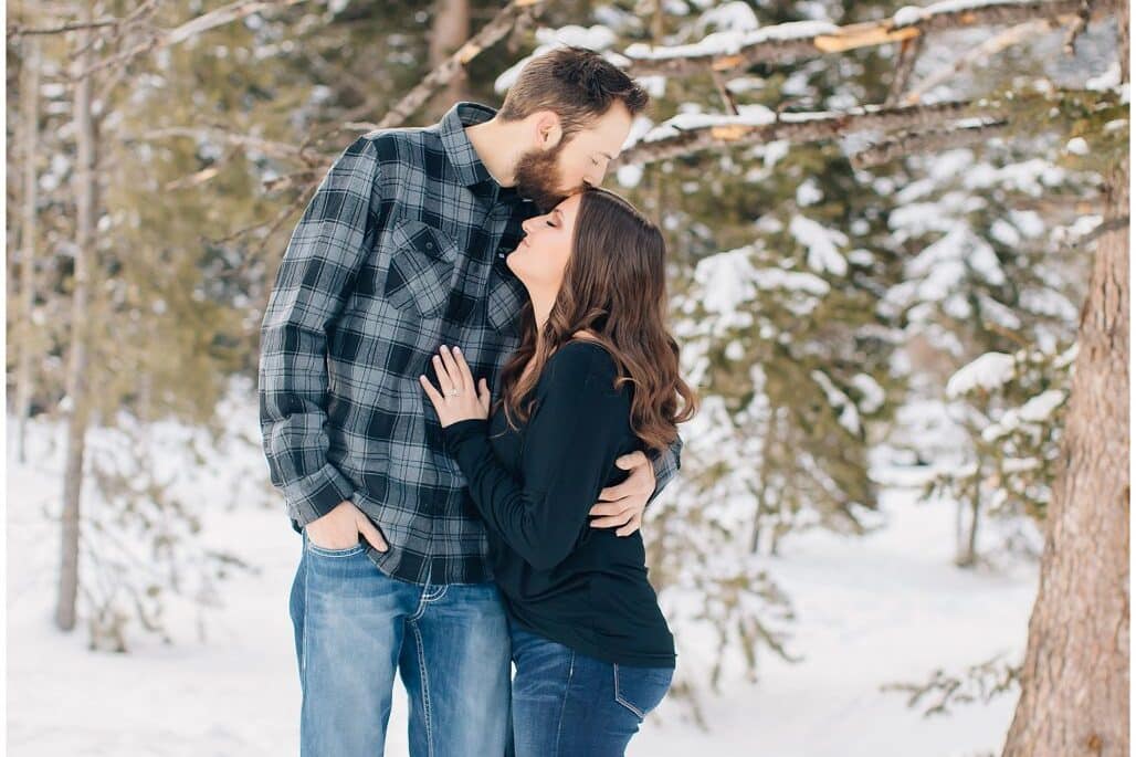 A man kissing his fiance on the forehead during their winter engagement photos | The Dating Divas